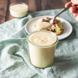A spoonful of sour cream sauce held over the jar with a tostada in the background