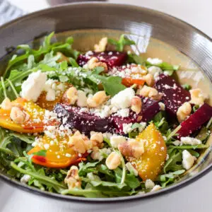 A brown bowl filled with salad with yellow and red beets, cheese and crumbled cheese - square
