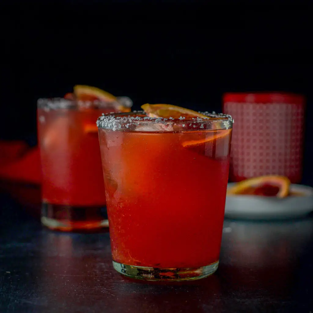 Vertical view of salted glasses blood margarita withe a slice of orange in the drink - square