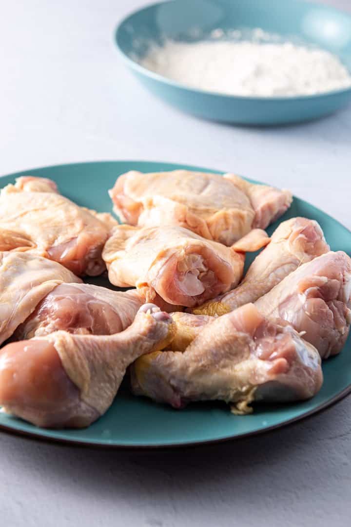 Chicken dried and on a plate with a bowl of flour in the background
