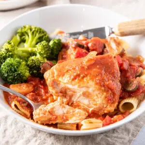 Square photo of the chicken in a red sauce on a white plate with broccoli