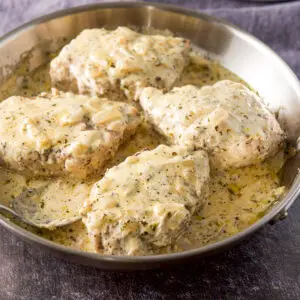 A silver pan of pork chops with a creamy sauce on them