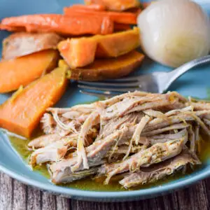 Close up of pork with gravy and carrots and onion on a plate with it