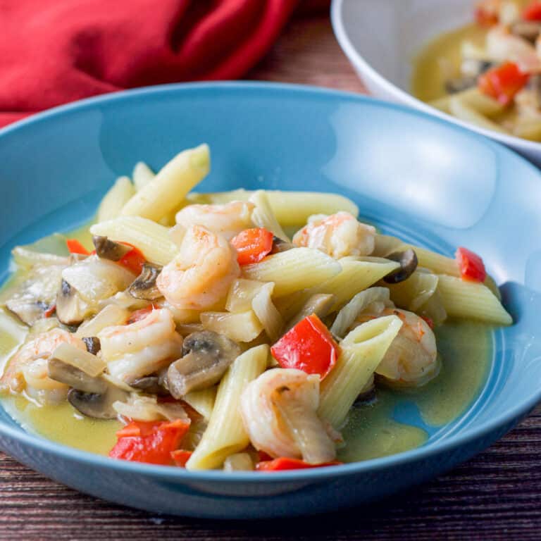 A blue bowl filled with shrimp scampi with a red napkin in the background