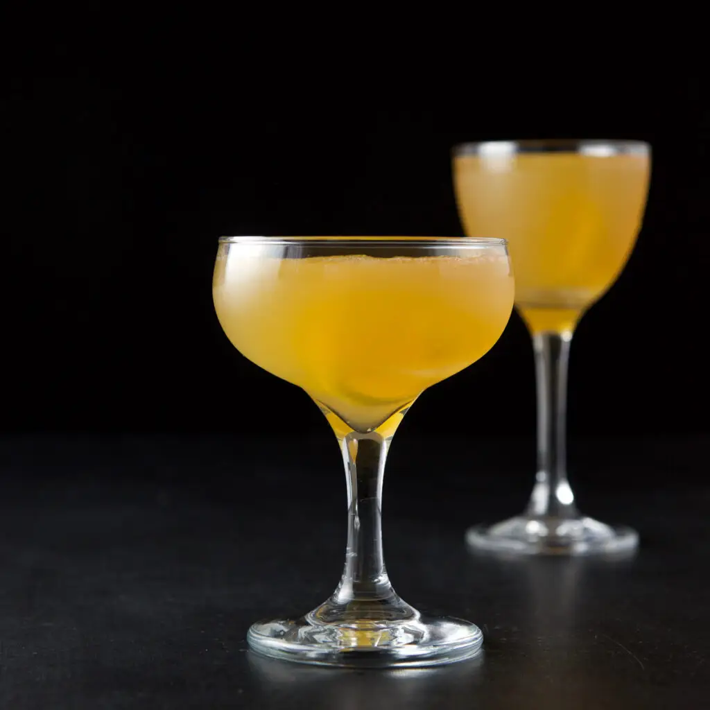A coupe glass filled with the sidecar cocktail in front of a taller martini glass - square