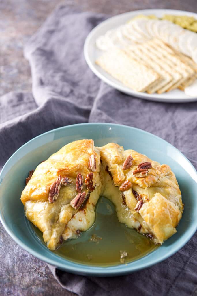 Cut baked brie with cheese oozing out and crackers in the background