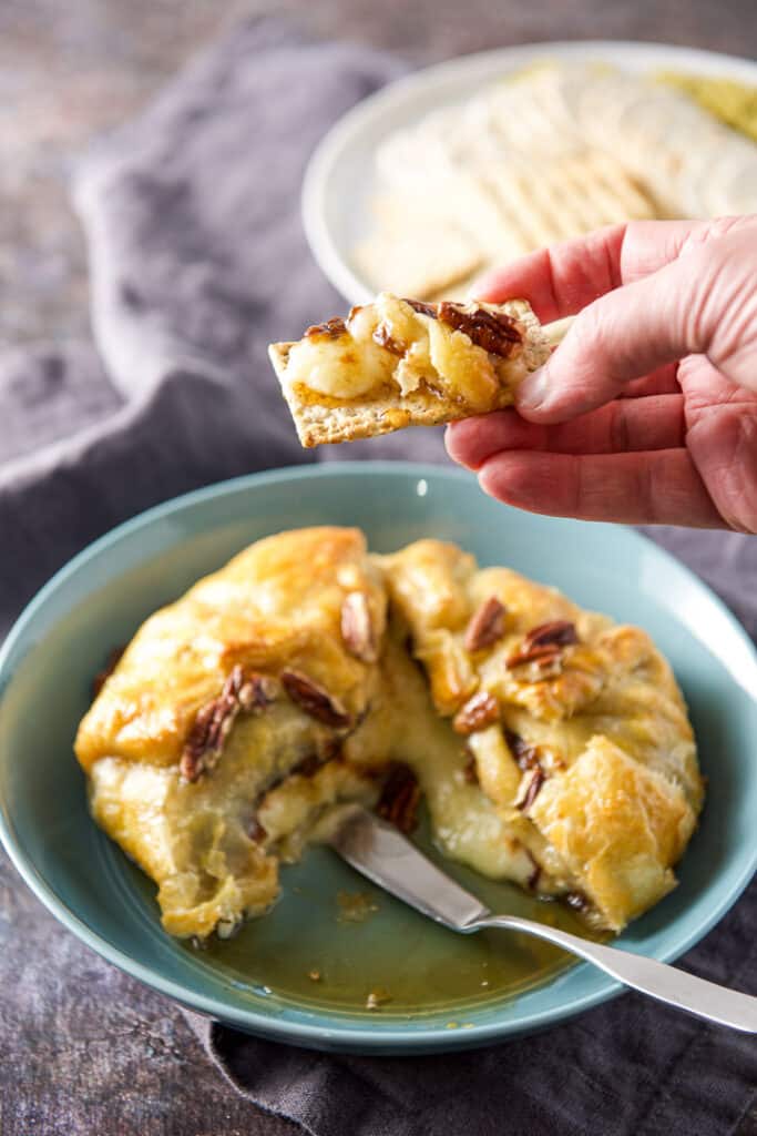 A hand holding a cracker with cheese on it over the bowl