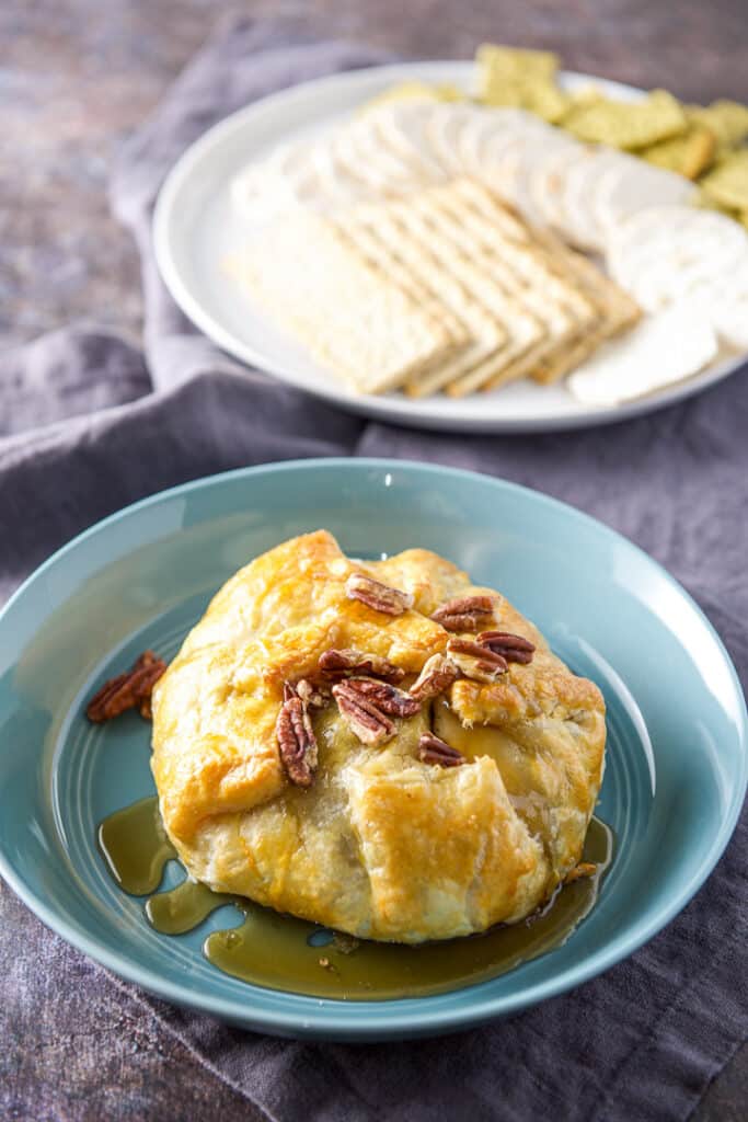 The whole brie in a blue bowl with maple syrup and crackers behind it
