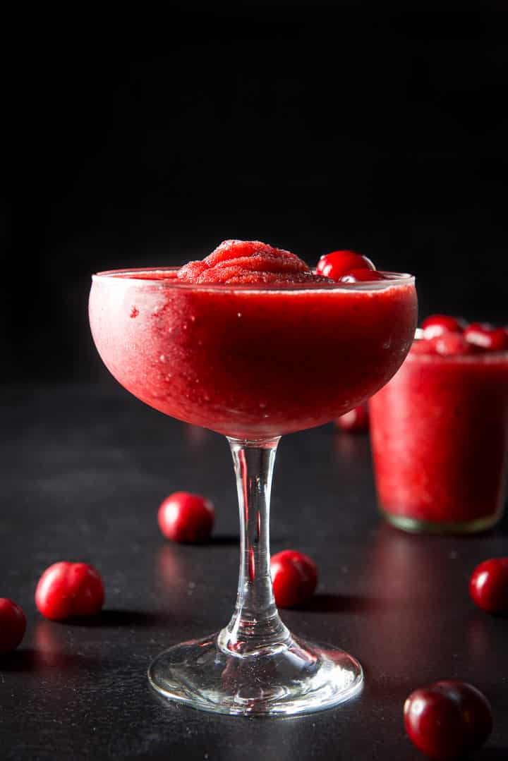Vertical view of the bowl glass filled with the cherry cocktail. The table is strewn with cherries