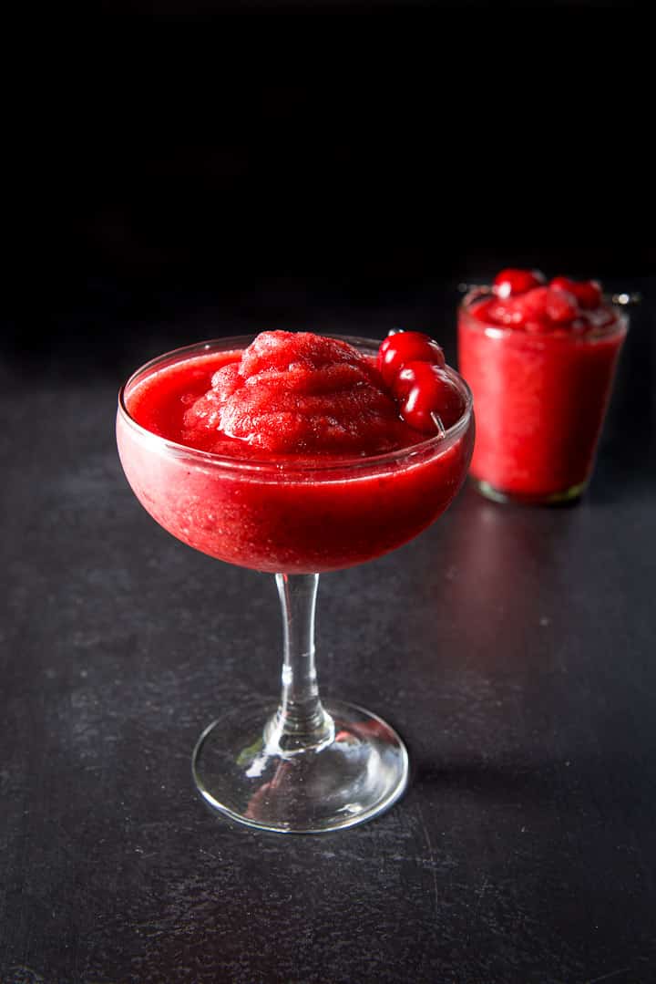 Bowl margarita glass overfilling with the frozen cherry marg with another glass off to the side