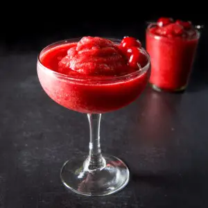 Cherries on a pick on the side of a margarita glass filled with frozen cherry margarita