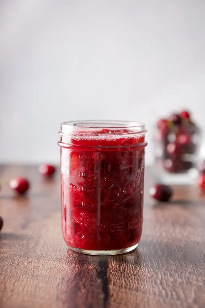 Vertical view of the sauce in a jar with cherries in the background
