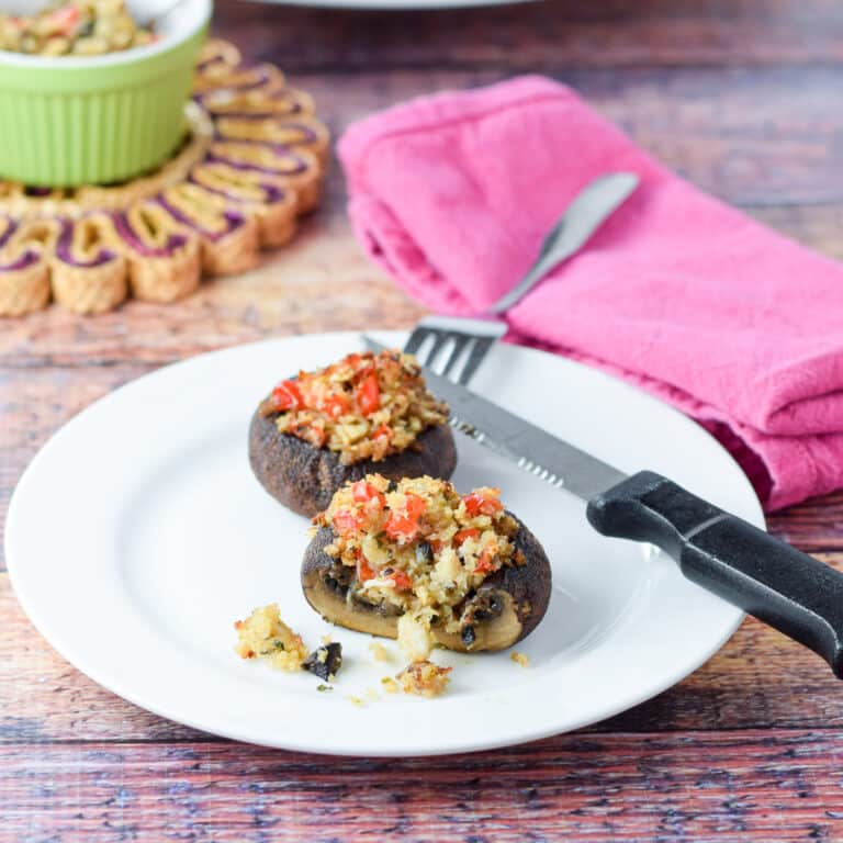 Two stuffed mushrooms on a white plate with a pink napkin and knife and fork. There is a slice taken out of the front mushroom