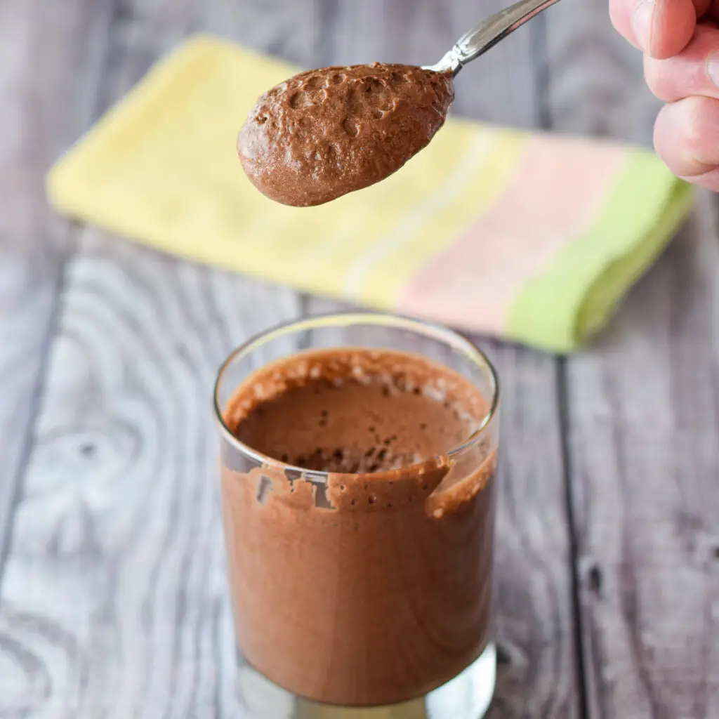 A spoon of velvety chocolate mousse over a glass of the dessert