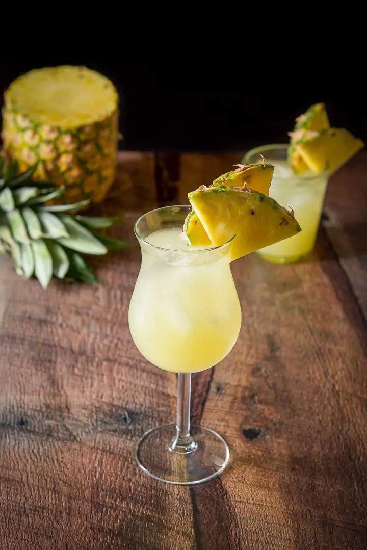 Tulip glass filled with the drink with two pineapple slices on the rim