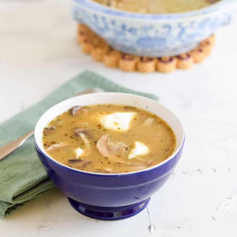 Mushroom soup in a blue bowl with sour cream in it. There is a lighter blue bowl filled with the soup in the background