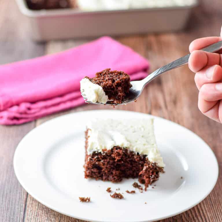 A fork holding a piece of chocolate cake above a plate