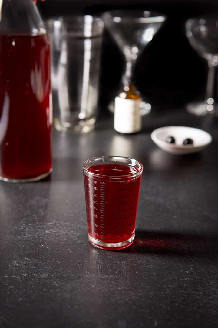 Cherry bourbon poured out with the bottle, cocktail shaker, cherries and glasses in the background