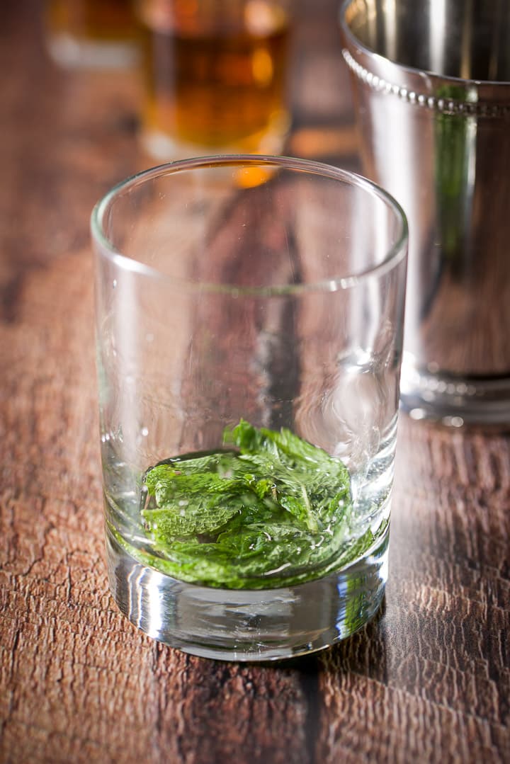 A clear glass and a stainless steel glass filled with the mint leaves and simple syrup muddled