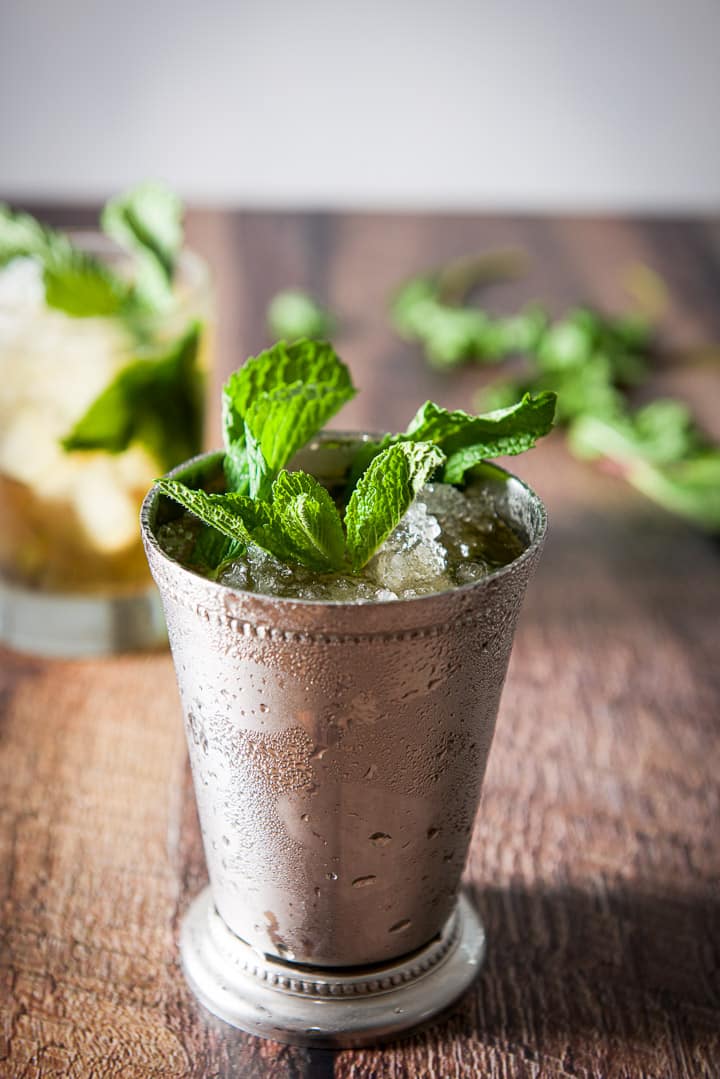 close up of the sterling silver glass filled with the julep in front of the clear glass and mint in the background