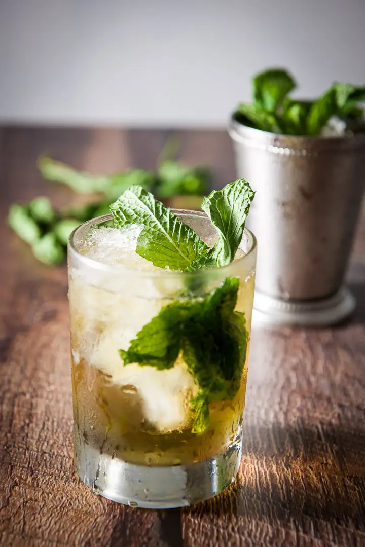 Clear glass filled with the julep with mint sticking out of it. The sterling silver glass is in the background