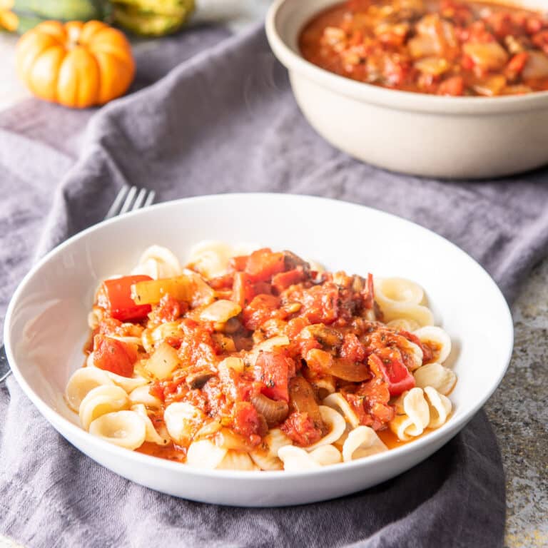 A shallow white bowl filled with pasta and gravy on a grey napkin with a bowl of gravy in the background