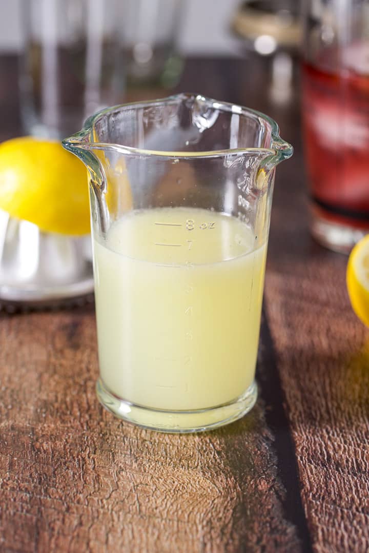Lemon juice measured out with a lemon and juicer, cocktail shaker and glasses in the background