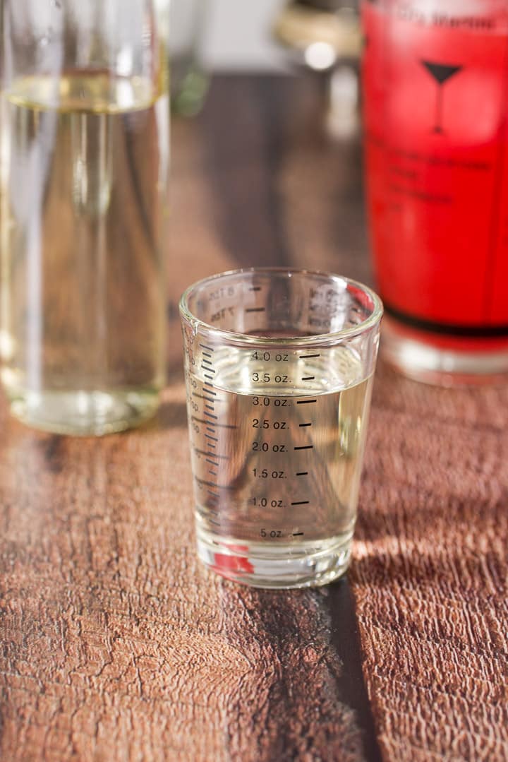 Simple syrup measured out with the bottle and cocktail shaker in the background