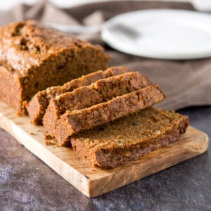 Slices of zucchini bread on a wooden board with a plate in the background - square