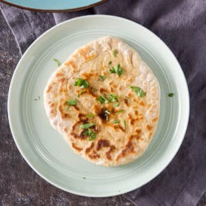 Overhead view of a piece of naan with butter and cilantro on it - square