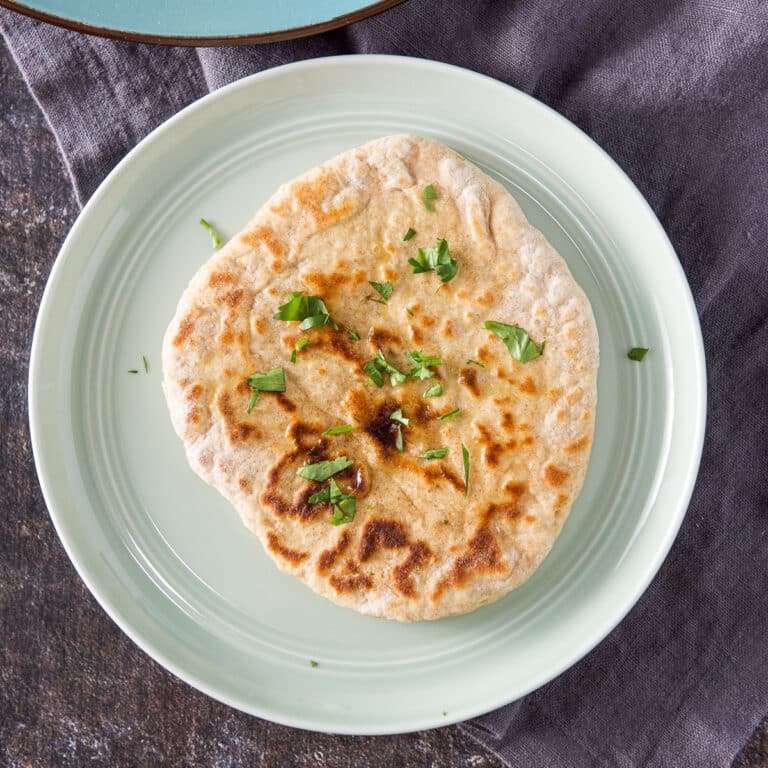 Overhead view of a piece of naan with butter and cilantro on it - square