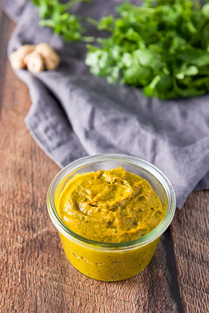 Curry in a glass jar with a napkin, cilantro and ginger in the background