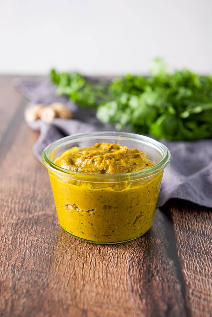 Curry paste in a jar on a wooden table with a bunch of cilantro