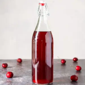 A tall bottle of cherry vodka with cherries on the table - square