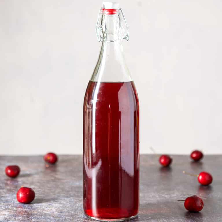A tall bottle of cherry vodka with cherries on the table - square