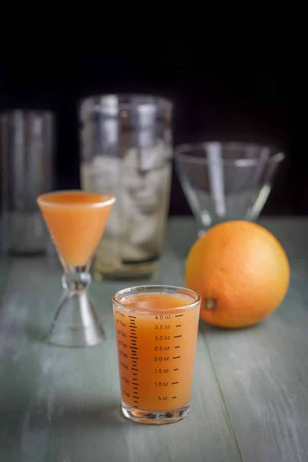 grapefruit juice measured out with a grapefruit, shaker and glasses in the background