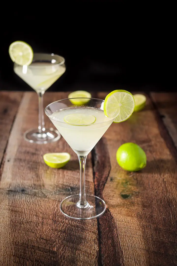A beveled regular martini glass with another fun glass filled with the martini and garnished with lime wheels