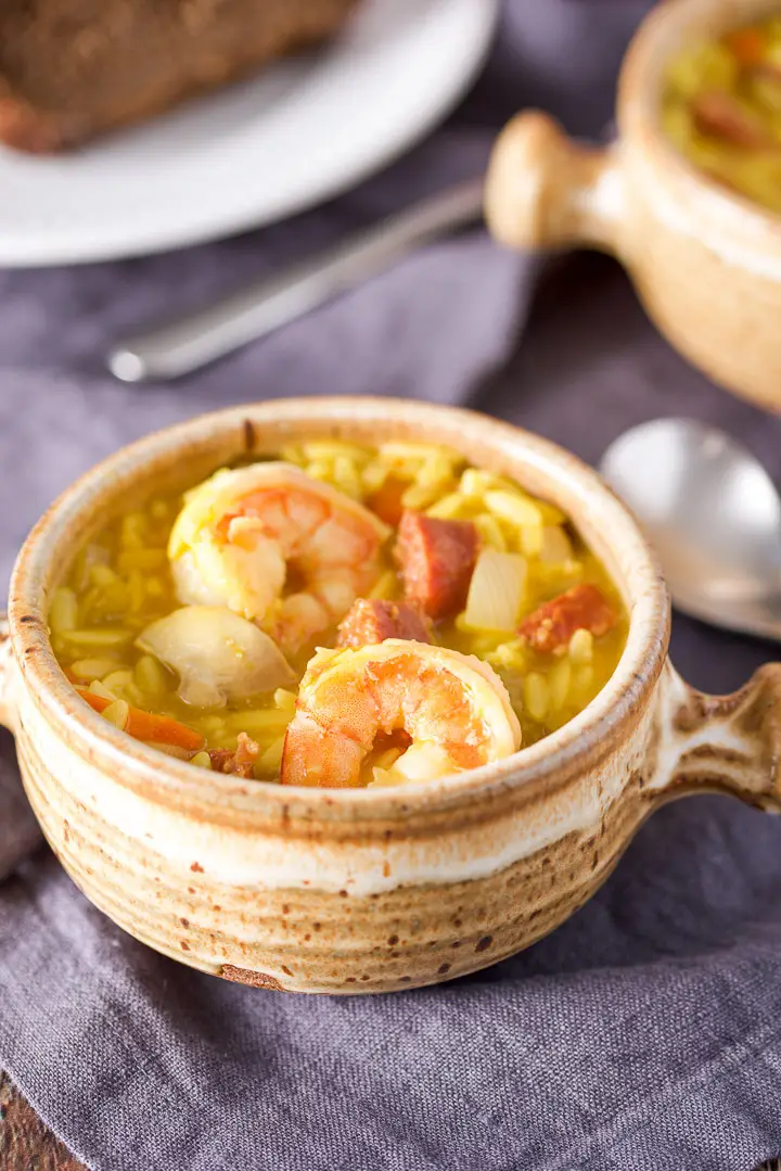 Close up of a beige crock with two shrimp, chorizo and orzo soup