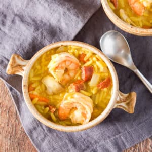 Overhead view of a crock with handles with the soup in it. There are two pieces of shrimp, chicken and chorizo showing