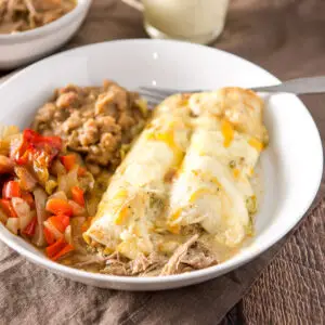 A white bowl with enchiladas with a cream sauce and beans and vegetable - square
