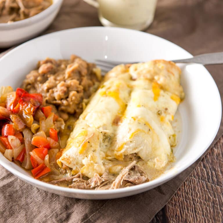 A white bowl with enchiladas with a cream sauce and beans and vegetable - square