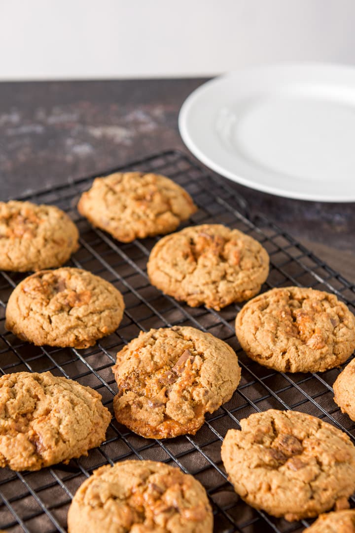 Cookie on a wire rack with one of the cookies with a melted candy bar - showing an irregular shape
