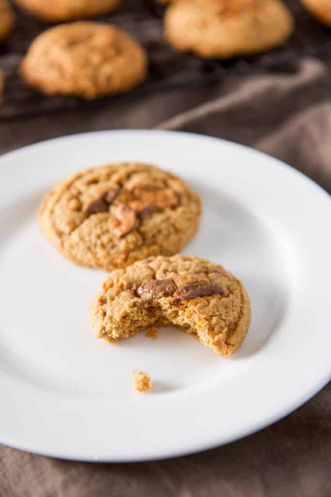 A bite taken out of one of the cookies on a white plate with more cookies in the background