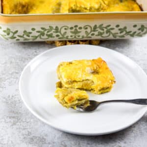 A forkful of chile relleno resting on a plate with the baking dish in the background - square