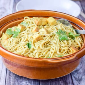 Tofu on noodles with cilantro sprinkled on it in a big brown bowl