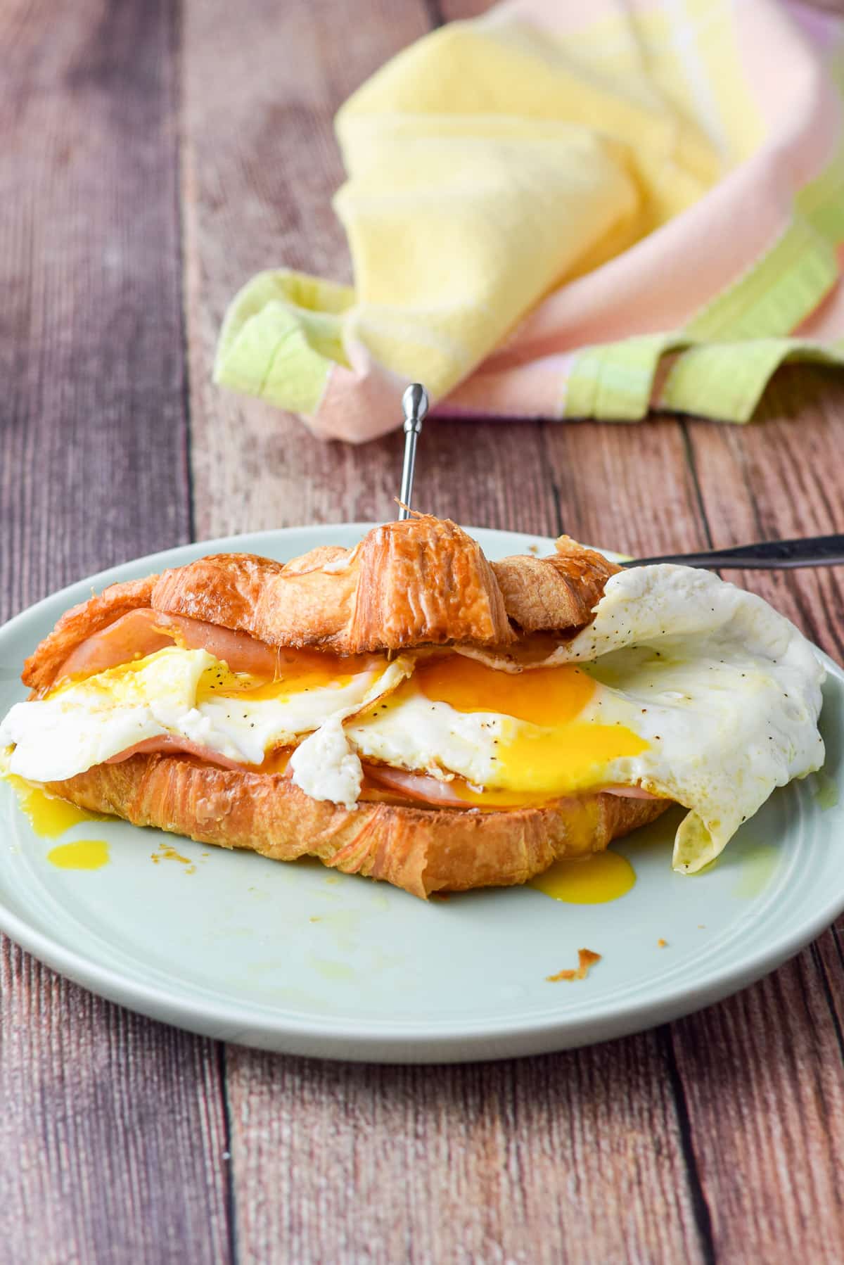 A croissant holding eggs, cheese and ham. The yolk has been broken and is dripping