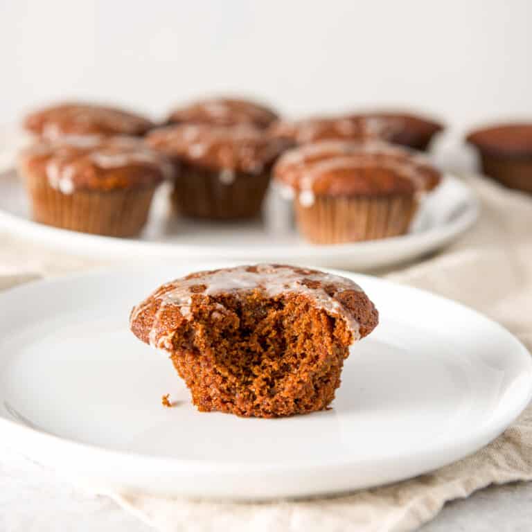 Ginger muffin on a plate with a bite taken out with a big plate of muffins in the background