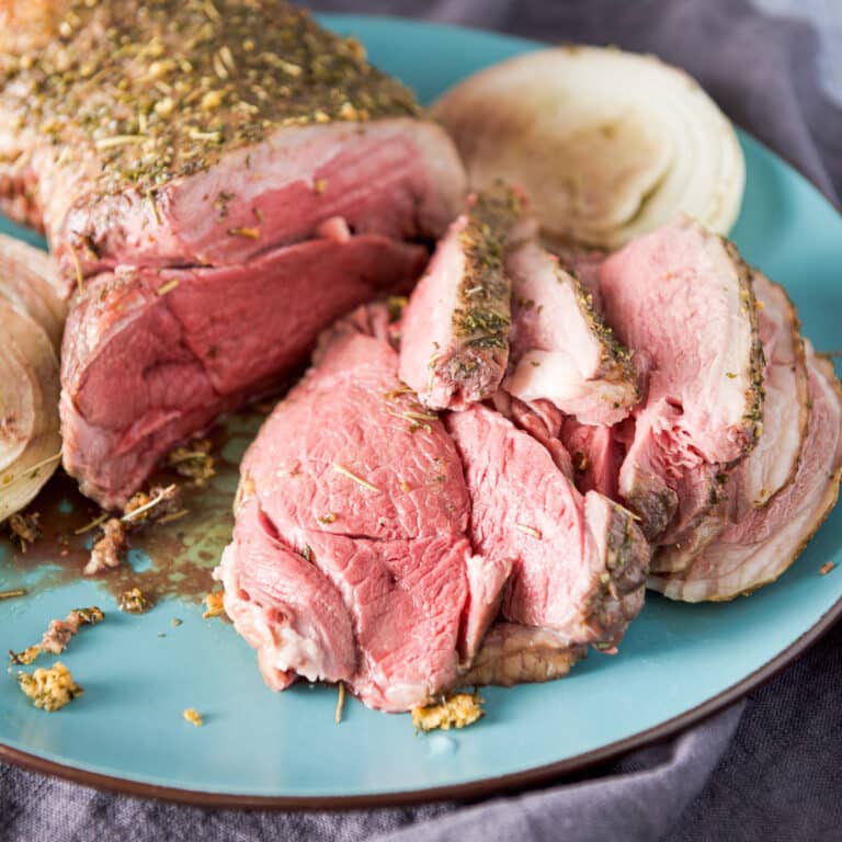 A blue platter with sliced lamb, juice and onion slices - square