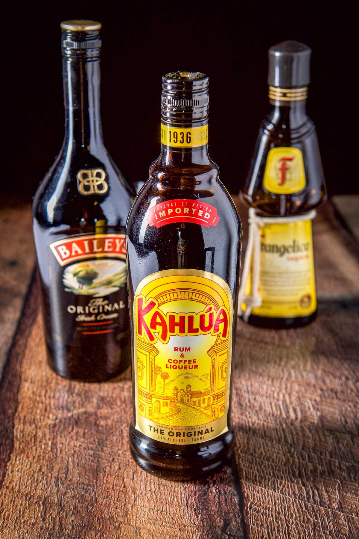 Kahlua, Baileys Irish cream and Frangelico on a wooden table