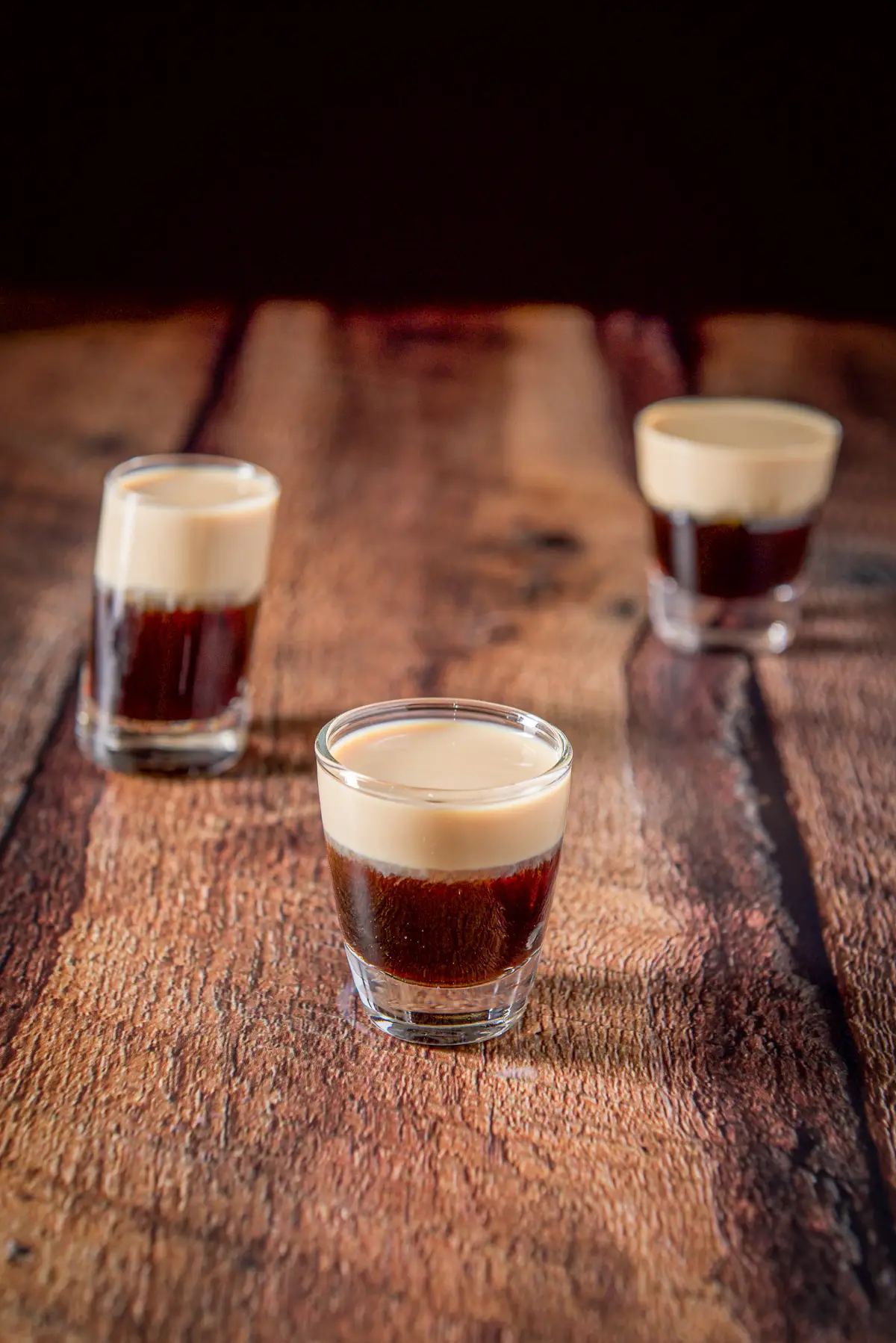 Three glasses filled with a layered shot all on a wooden table